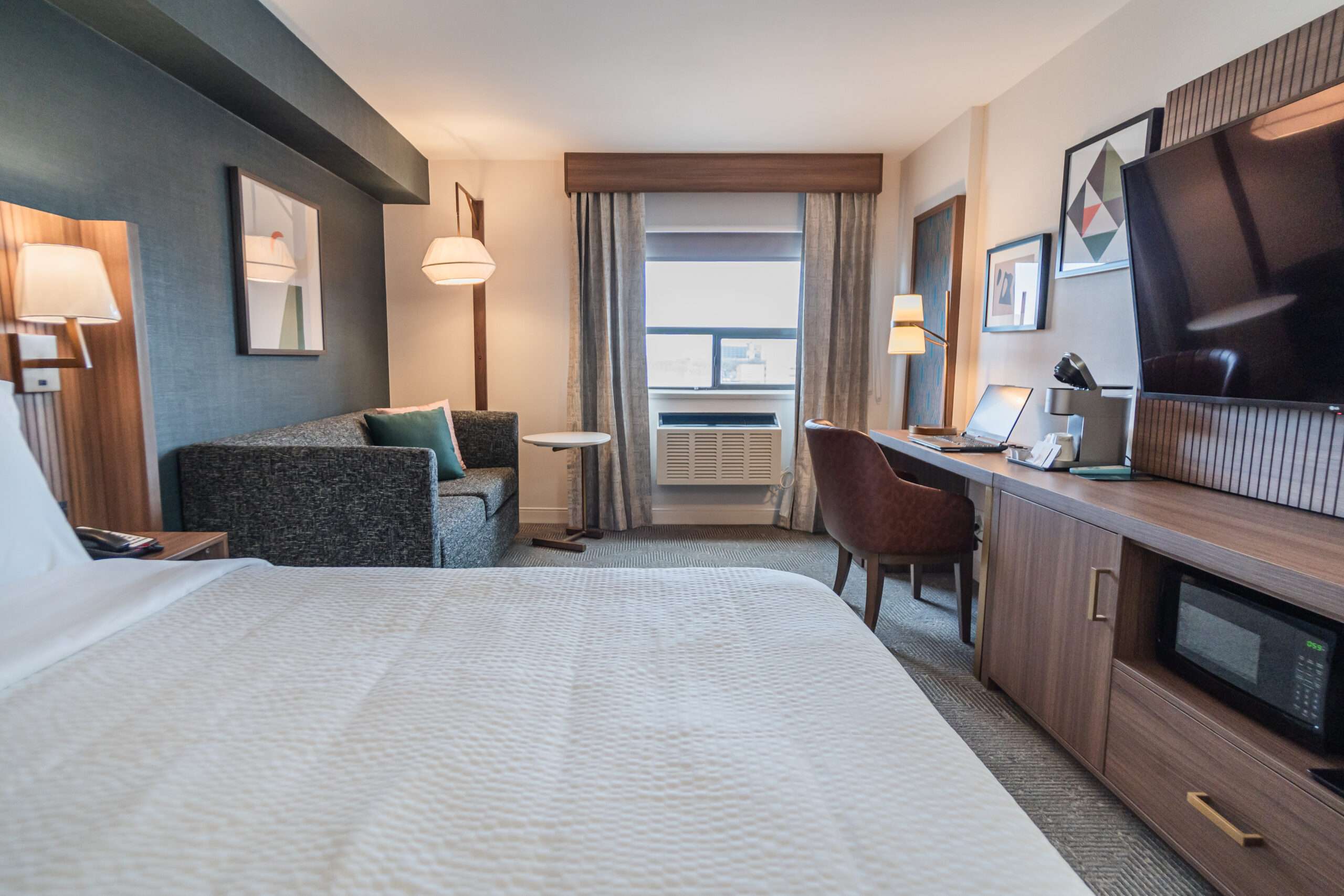 A hotel room with a bed, desk and couch- Canadian hotel room