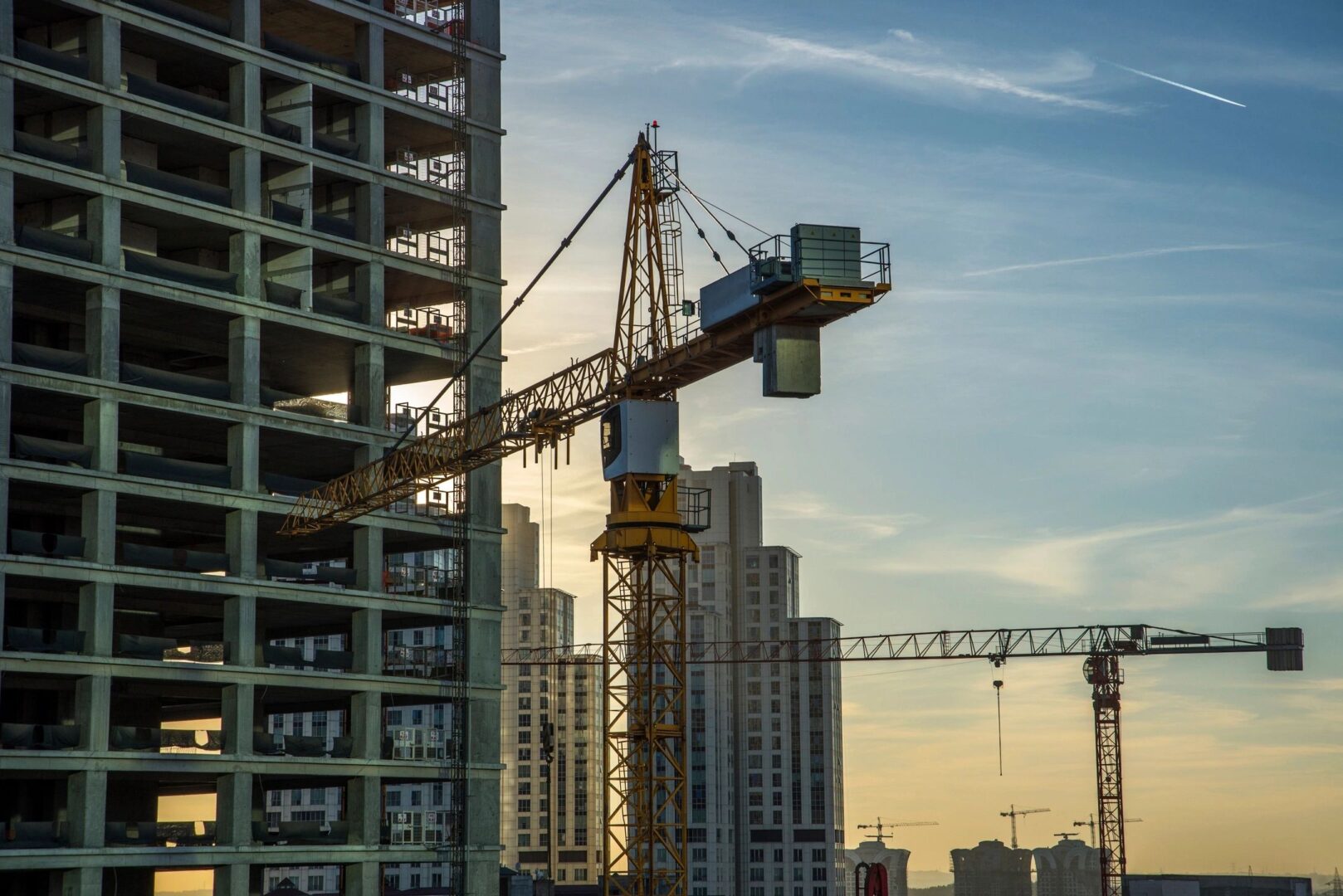 A crane builds a hotel building against a beautiful orange sunset.
